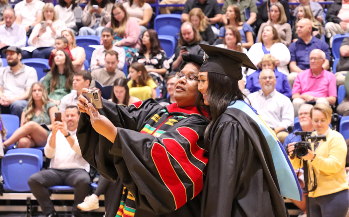 UNK professor taking a selfie with a UNK graduate student during UNK's commencement ceremony.