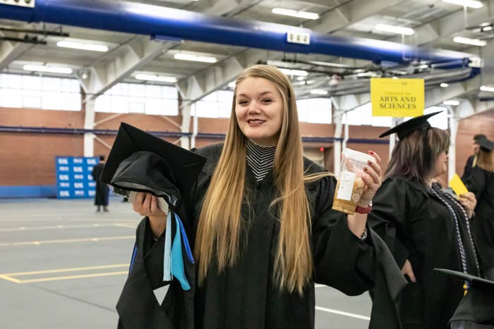 Woman with long blond hair holding a to-go coffee cup in her graduation regalia at UNK's graduation ceremony.