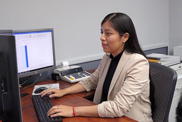 A woman working at a desk on a computer, focusing on a spreadsheet, in a professional office setting.