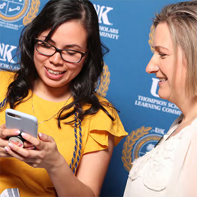 student with phone in hand talking with alumni