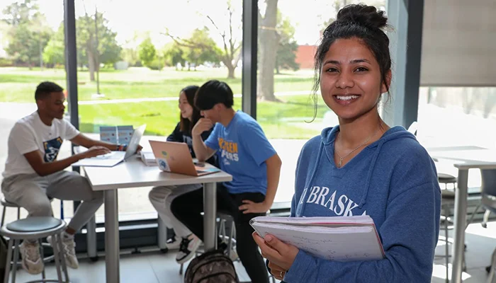 a student poses for a photo with more students at a table behind her