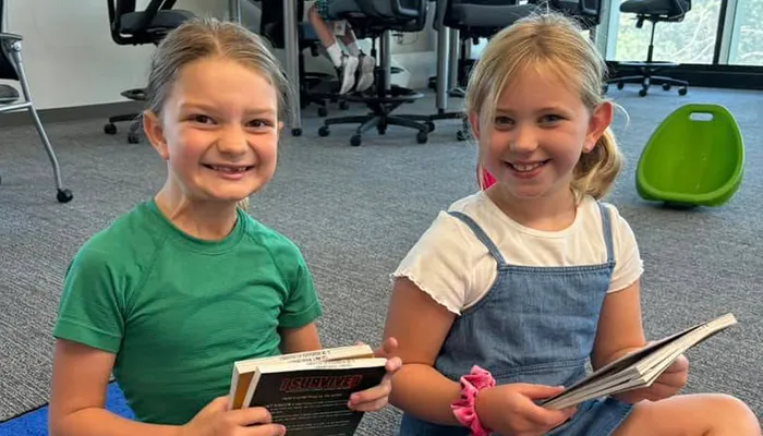 two students hold books and smile for a photo