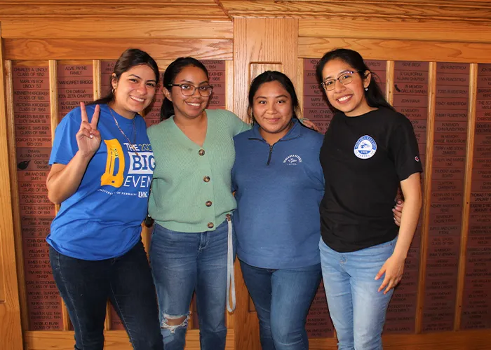 trio students pose for a photo in front of a wood paneled wall