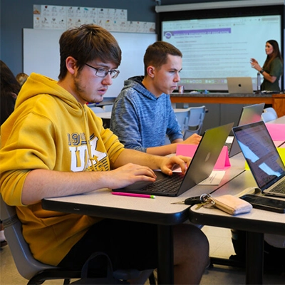 students sit at a table on their laptops during a class