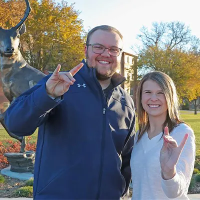 two students throw the lopes in front of the loper statue