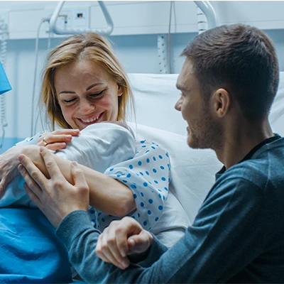 a woman sits in a hospital bed holding a newborn baby while a man sits next to them