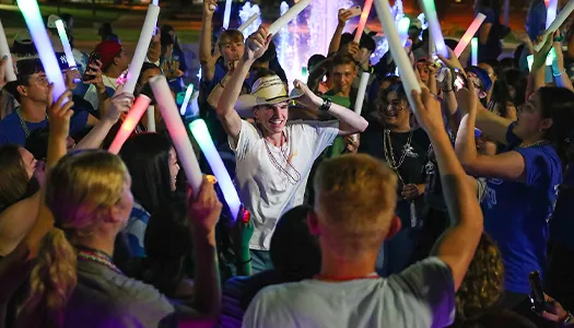 students wave glow sticks and dance at a concert
