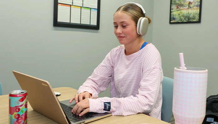 a student sits at a desk in the library typing on her computer