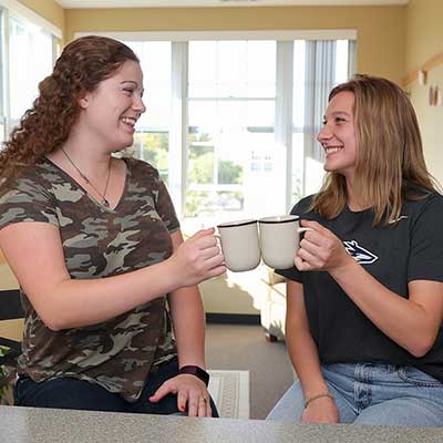 two students sit at a counter in their dorm and clink mugs