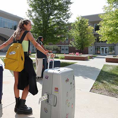a student rolls a suitcase outside her dorm