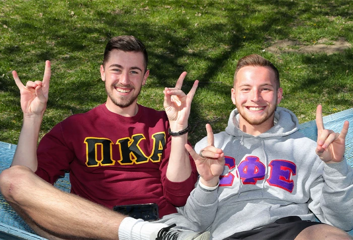 two students with greek life shirts throw their lopes