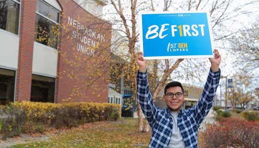 a first-generation student holds up a be first sign outside the student union