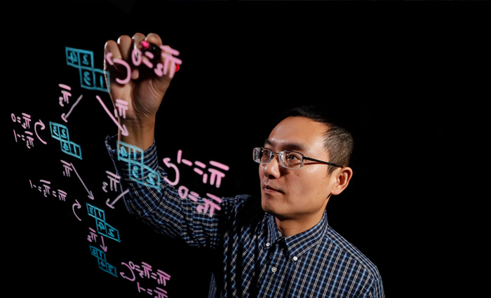 Professor Jia Juang writing equations on a marker board