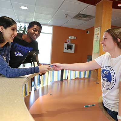 students talk to a worker at a Helpdesk inside a dorm lobby
