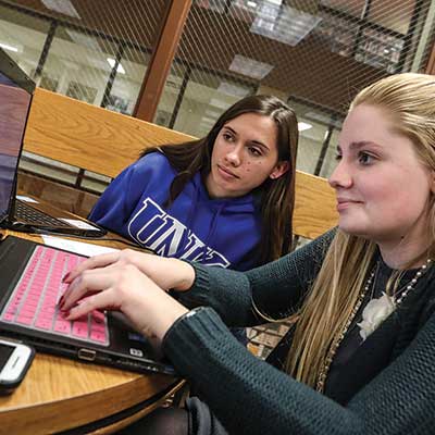 two students sit in front of a laptop