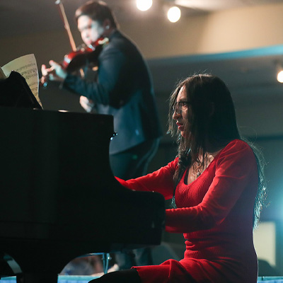 a woman in a red dress plays the piano during the FAME Talent show