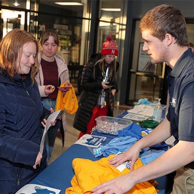 a unk employee hands out shirts to students at a welcome home week event 